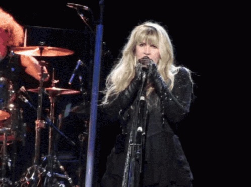 A Woman Singing Into A Microphone In Front Of A Drum Set GIF