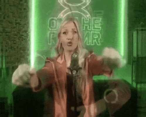 A Woman Singing Into A Microphone In Front Of A Green Sign That Says Oh He Mr. GIF