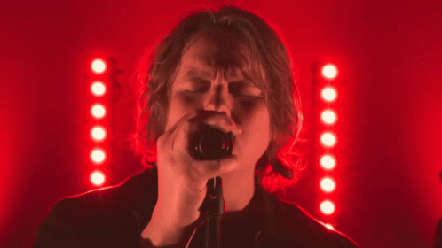 A Woman Singing Into A Microphone In Front Of A Red Background GIF