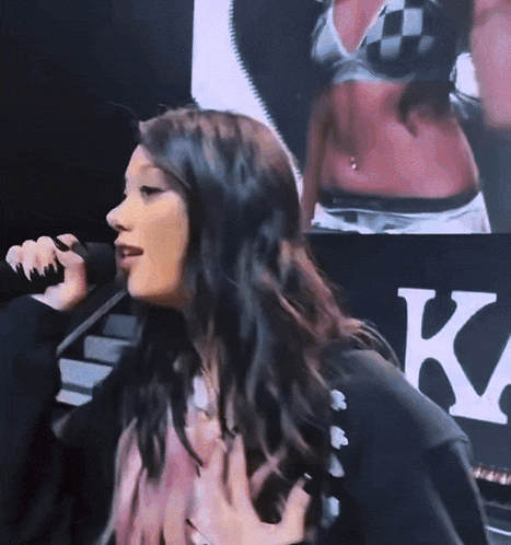 A Woman Singing Into A Microphone In Front Of A Sign That Says K. GIF