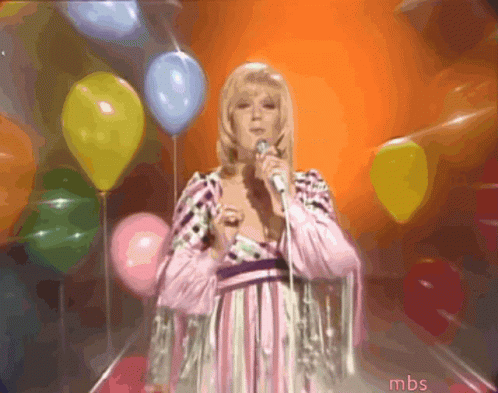 A Woman Singing Into A Microphone In Front Of Balloons With Mbs Written On The Bottom GIF