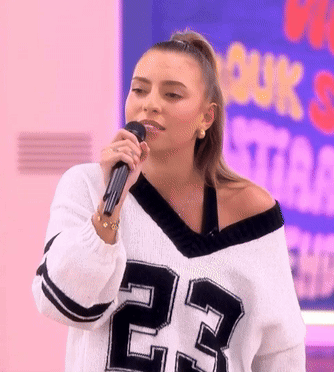 A Woman Singing Into A Microphone Wearing A Jersey With The Number 23 On It GIF