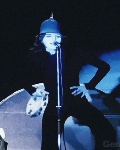 A Woman Singing Into A Microphone While Holding A Tambourine In Front Of Her GIF