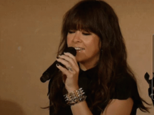A Woman Singing Into A Microphone While Wearing A Bracelet With Spikes GIF