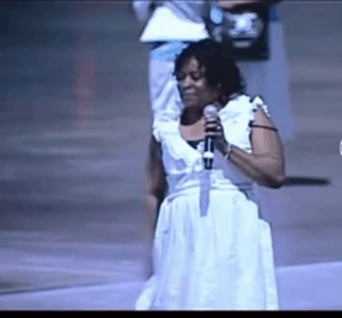 a woman singing into a microphone while wearing a white dress