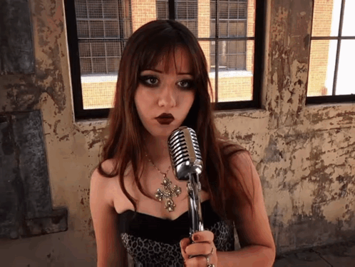 A Woman Singing Into A Microphone With A Cross Necklace GIF