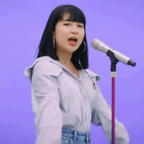 A Woman Singing Into A Microphone With A Purple Background Behind Her GIF