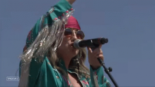 A Woman Singing Into A Microphone With A Sign That Says Stagecoach On It GIF
