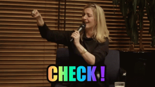 A Woman Singing Into A Microphone With Check Written In Rainbow Colors Behind Her GIF