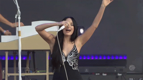 A Woman Singing Into A Microphone With Her Arms Outstretched GIF