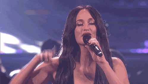 A Woman Singing Into A Microphone With Her Hand On Her Face GIF