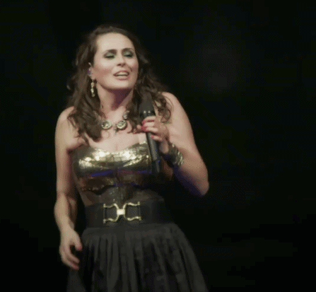 A Woman Singing Into A Microphone With The Words Een Beetje Warm He On The Bottom GIF