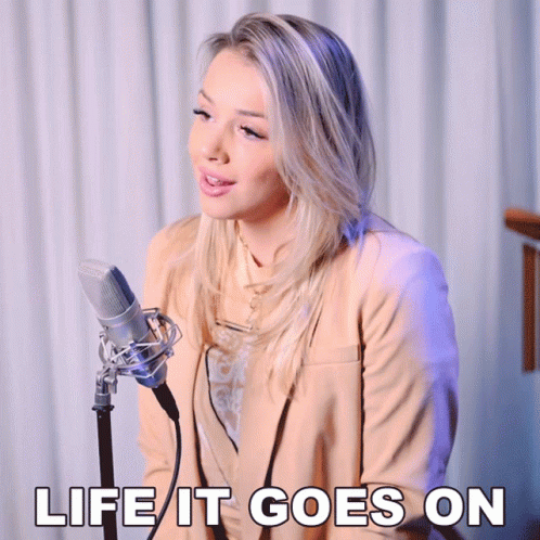 A Woman Singing Into A Microphone With The Words " Life It Goes On " Above Her GIF