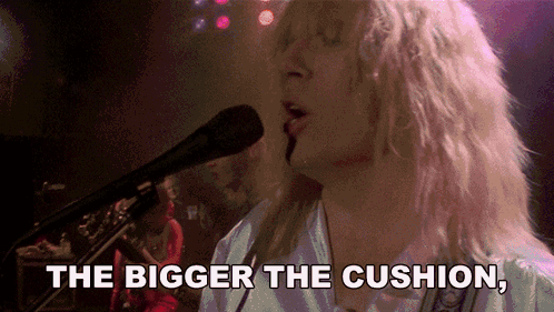 A Woman Singing Into A Microphone With The Words " The Bigger The Cushion " Above Her GIF
