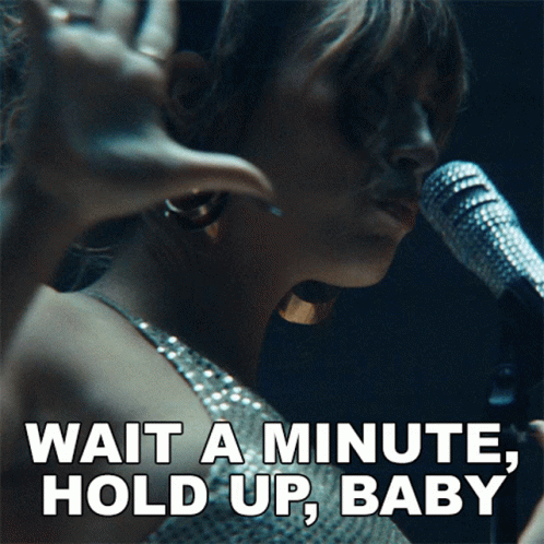 A Woman Singing Into A Microphone With The Words " Wait A Minute Hold Up Baby " Below Her GIF