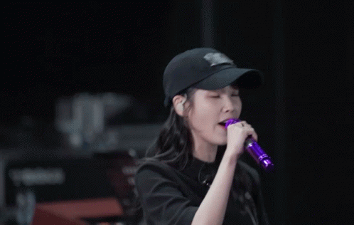 a woman singing into a purple microphone wearing a baseball cap