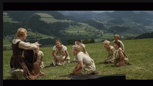 A Woman Singing To A Group Of Children On A Hill GIF