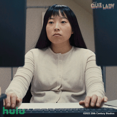 A Woman Sits At A Desk In Front Of A Computer Screen With The Words Quiz Lady Written Above Her GIF