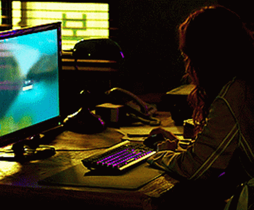 A Woman Sits At A Desk Playing A Video Game On A Computer GIF