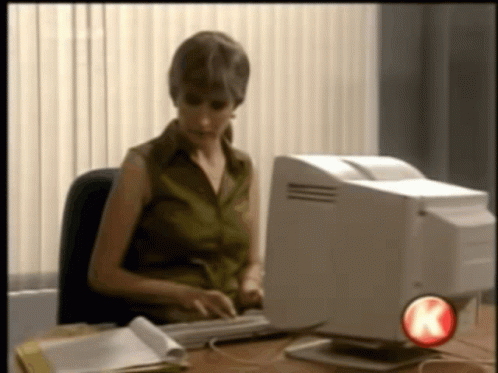 A Woman Sits At A Desk Typing On A Keyboard In Front Of A Computer With A Red K On The Bottom Right GIF
