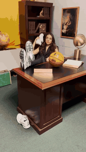 A Woman Sits At A Desk With Her Feet Up And A Basketball On The Desk With A Sign That Says Basketball Coach GIF
