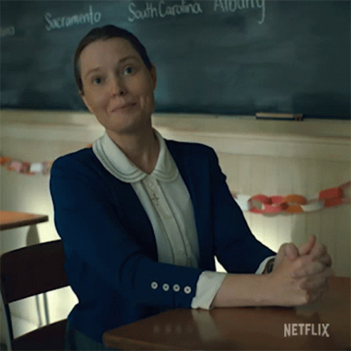 A Woman Sits At A Desk With Her Hands Folded In Front Of A Blackboard That Says South Carolina On It GIF