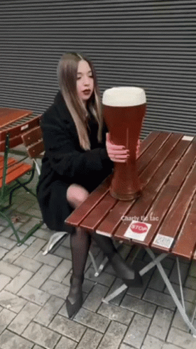 A Woman Sits At A Table Holding A Giant Beer Glass GIF