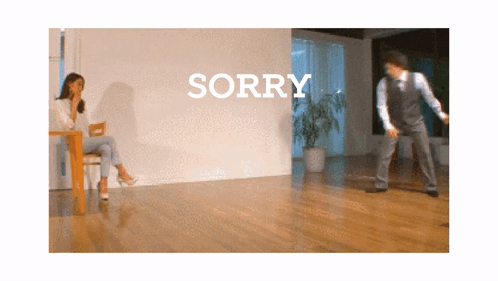 Woman Sitting At Table While Man Dances In Front Of Sorry Wall GIF