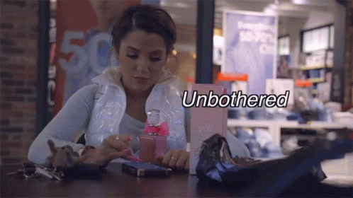 A Woman Sits At A Table With A Bottle Of Perfume And The Word Unbothered Written Above Her GIF