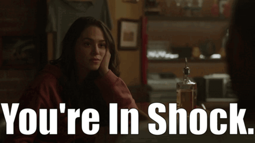 A Woman Sits At A Table With A Bottle Of Whiskey And The Words " You 'Re In Shock " Above Her GIF