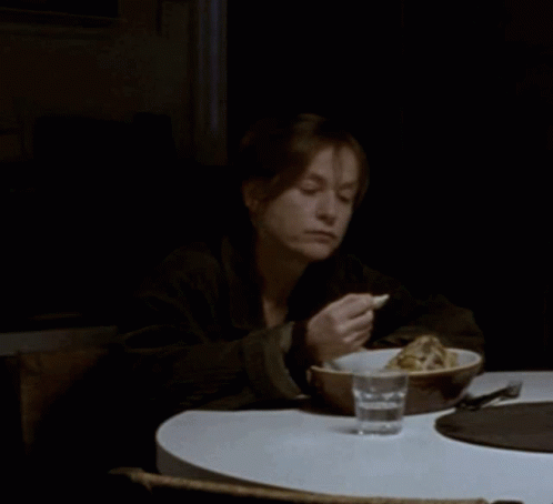 A Woman Sits At A Table With A Bowl Of Food And A Glass Of Water In Front Of Her GIF
