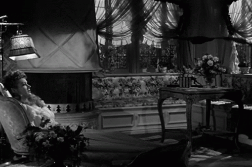 A Woman Sits In A Chair In Front Of A Fireplace In A Black And White Photo GIF