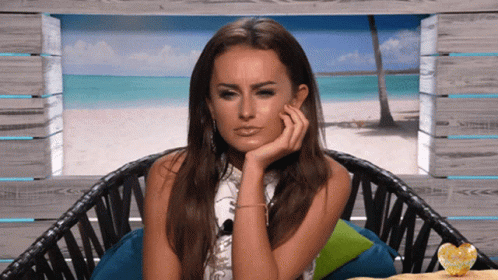 A Woman Sits In A Chair With Her Hand On Her Face GIF