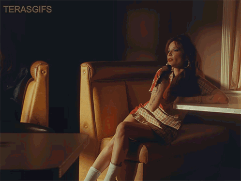 A Woman Sits In A Diner Booth With A Microphone In Her Hand And The Words Terasgifs Below Her GIF