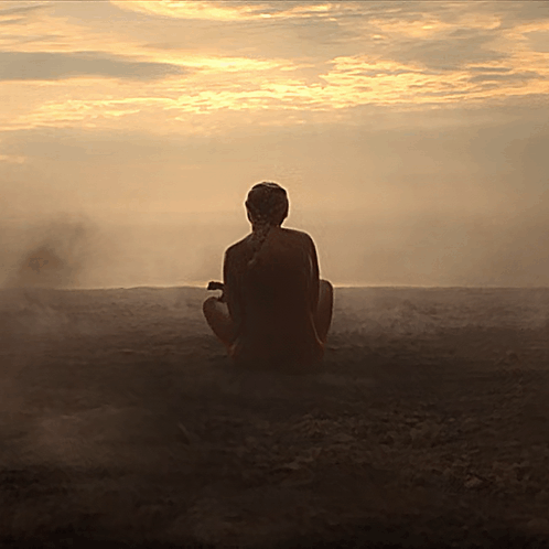 a woman sits in a lotus position in front of a sunset sky