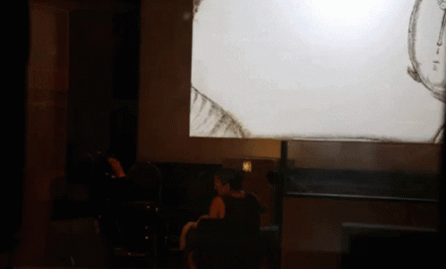 A Woman Sits In Front Of A Projector Screen That Shows A Drawing GIF