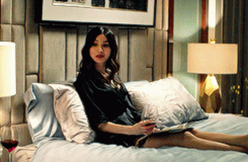 A Woman Sits On A Bed Reading A Magazine GIF