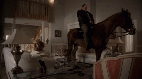 A Woman Sits On A Couch In A Living Room With Two Lamps GIF