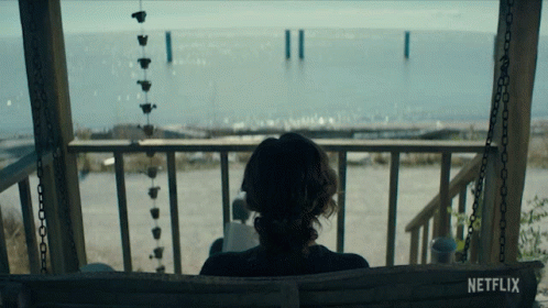 A Woman Sits On A Porch Swing With A Netflix Logo Visible GIF