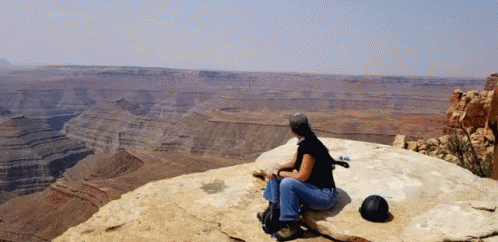A Woman Sits On A Rock Overlooking A Desert Landscape GIF