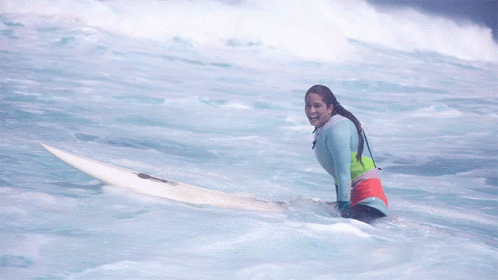 A Woman Sits On A Surfboard In The Ocean And Smiles GIF