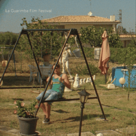 A Woman Sits On A Swing With The Words La Guarimba Film Festival Written Above Her GIF