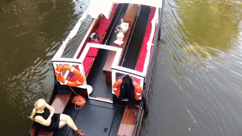 A Woman Sits On The Deck Of A Boat With A Life Preserver Attached To It GIF