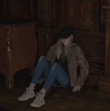 A Woman Sits On The Floor Wearing A Hat And Jeans GIF