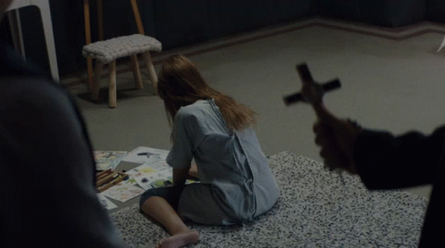 A Woman Sits On The Floor While A Man Holds A Cross In Front Of Her GIF