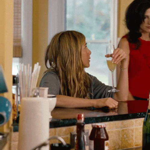A Woman Sitting At A Counter With A Glass Of Wine In Her Hand GIF