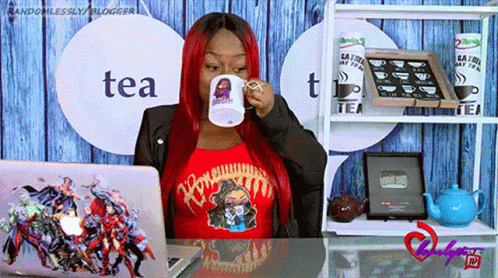 A Woman Sitting At A Desk Drinking From A Mug That Says Tea On It GIF