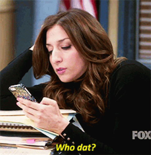 A Woman Sitting At A Desk Looking At Her Phone With The Caption Who Dat GIF