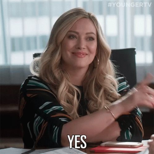 A Woman Sitting At A Desk Says Yes With Her Hands GIF