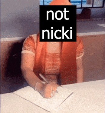 A Woman Sitting At A Desk With A Sign That Says Not Nicki On Her Face GIF
